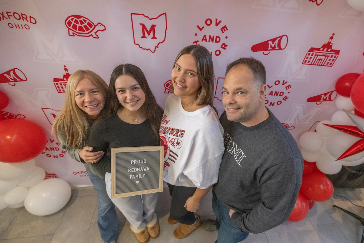 A family of four gathers round a " Proud Redhawk Family" Sign